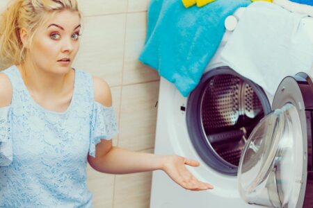 Une femme confuse devant une machine à laver ouverte